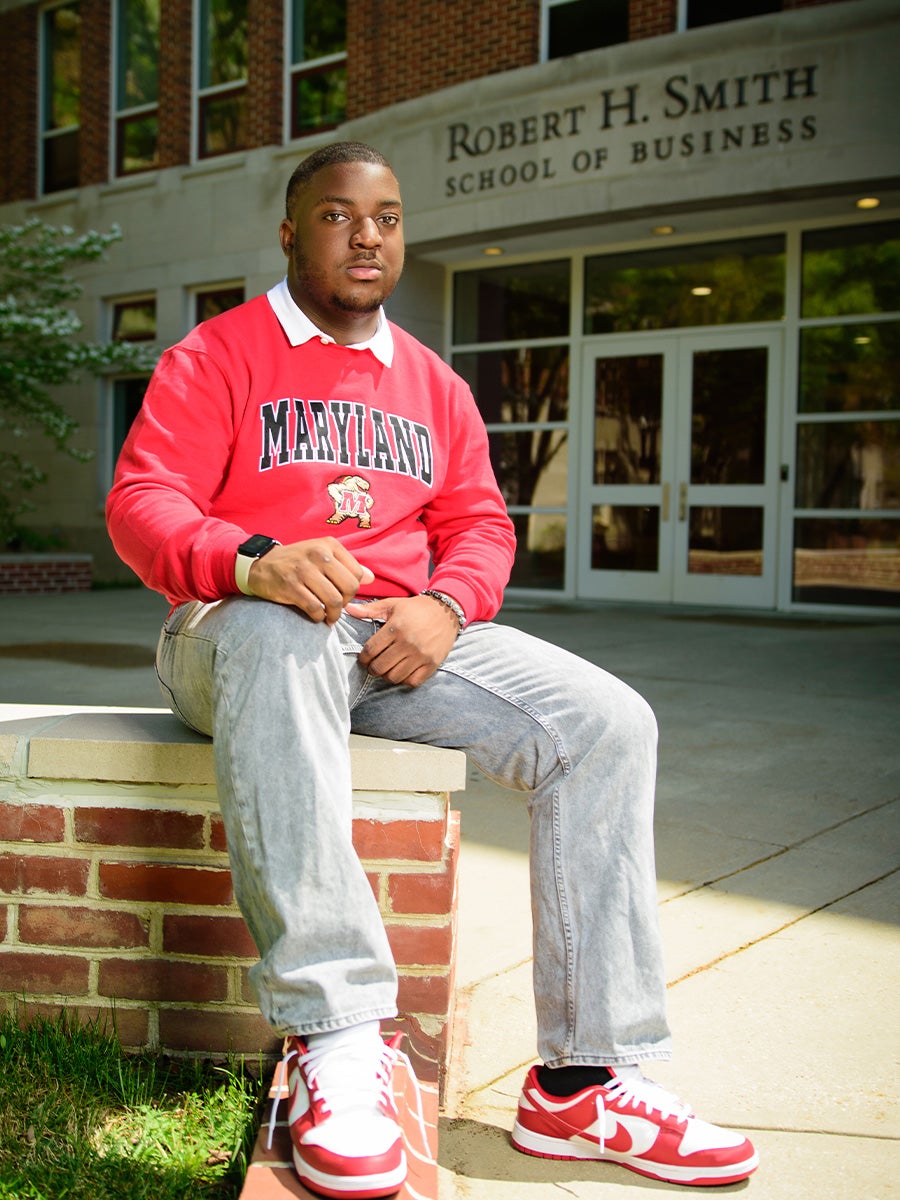 Adun's headshot is him sitting on a brick surface in front of the Smith Business School. He is wearing a read Maryland pull over 