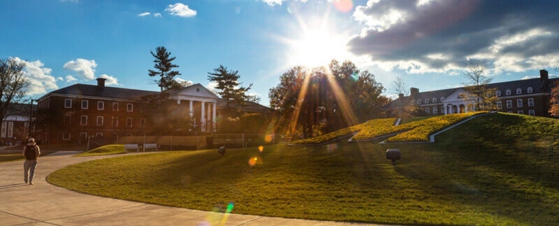 The sun is shining as a student walks by a campus building
