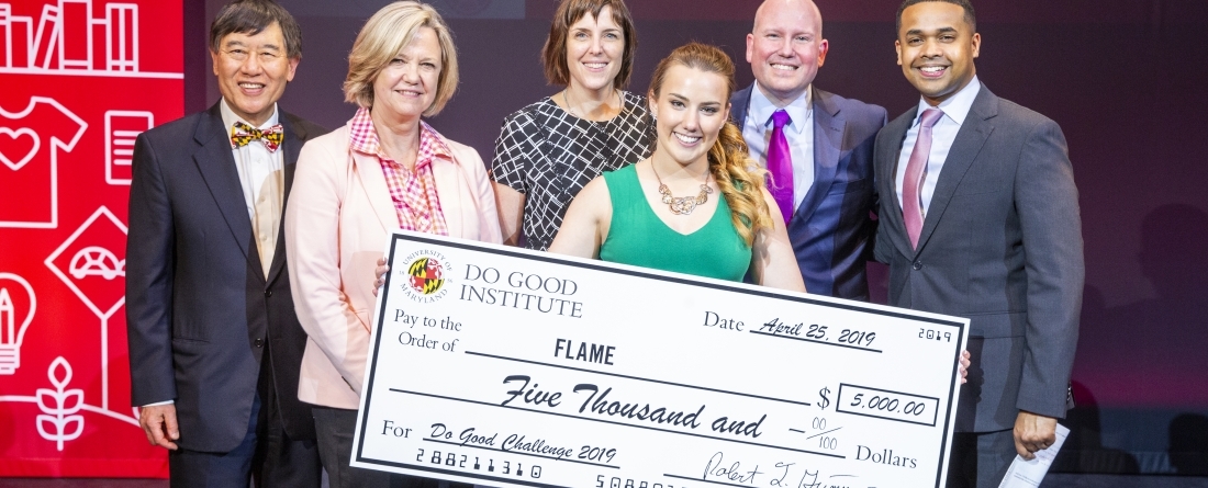 A group of people are standing on a stage, surrounding a woman holding a giant check for 5,000 dollars