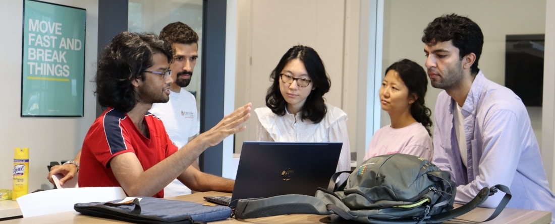 Students are sitting around tables in the Do Good Accelerator all looking at a computer screen and discussing 