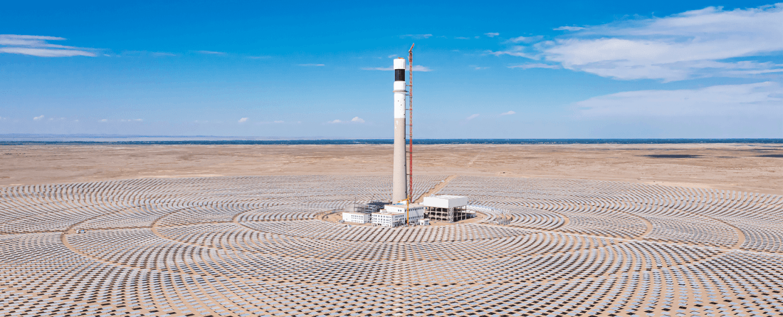 An aerial view of a solar farm with panels set up in circular panels around a tall tower on a clear day with blue skies.