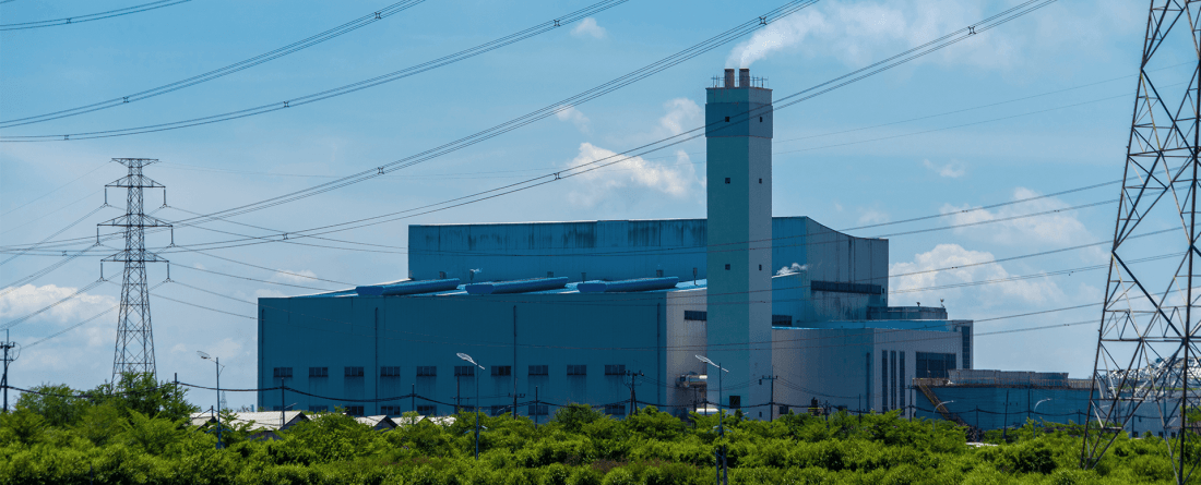 An energy facility with power lines and a marsh area in the foreground on a day with blue skies and clouds.