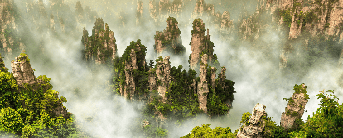 An aerial view of geologic formations peaking above fog with trees and greenery growing on the rocks.