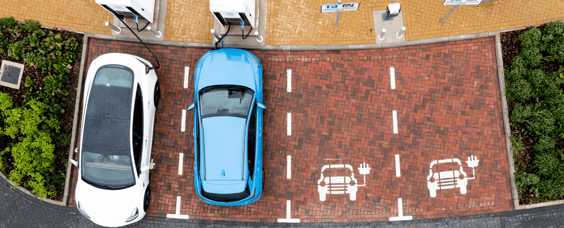 An aerial view of two electric vehicles plugged into a charging station with two open spots indicating parking for electric vehicles.