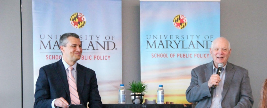 Image of Dean Gustavo Flores-Macias and Senator Ben Cardin sitting in front of 2 UMD School of Public Policy banners at a table having a talk