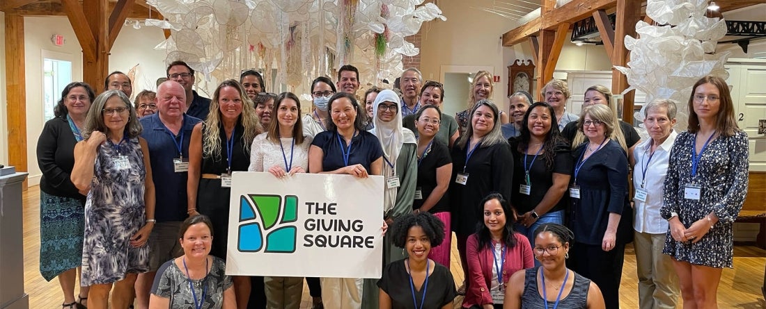 Group photo of people gathered together smiling and holding a banner that says The Giving Square.