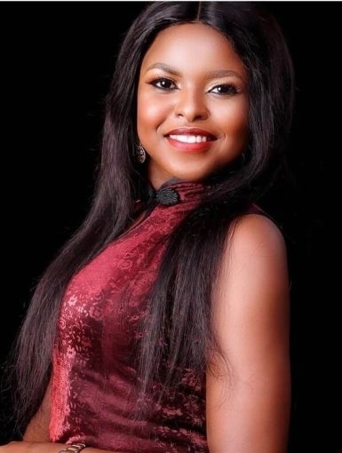 Enwongo is wearing a red dress and smiling at the camera. 